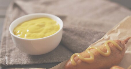 Showing corn dog on stick sitting on tabletop, white bowl of mustard on napkin, copy space