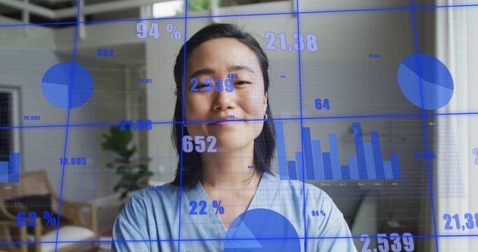 Standing Korean woman in light blue blouse presenting blue data charts in home office, with labels