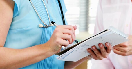 Writing clinician in blue scrubs completing medical forms at clinic, with clipboard and stethoscope