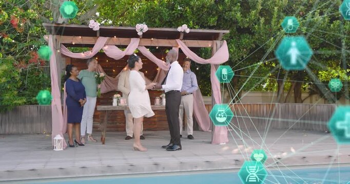 Couple moving closer, exchanging wedding rings, guests clapping, teal hexes drifting behind