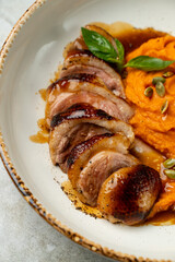 A beautifully arranged dish featuring tender duck breast slices paired with creamy sweet potato puree, topped with fresh basil and crunchy seeds, creating a feast for the senses