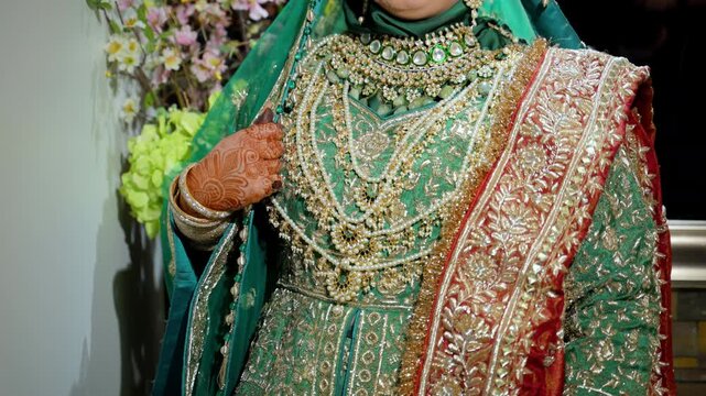 Green and gold colors in traditional wedding Indian or Pakistan clothes, Close up view of embroidered dress and henna painted hands on it