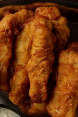 Crispy fried chicken strips rest on a dark platter, showcasing their golden texture, inviting hungry diners to enjoy a flavorful feast during a casual gathering