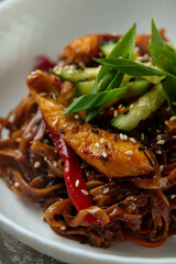 Savory stir-fried noodles glisten under ambient light, with golden chicken chunks, bright red peppers, and green scallions creating a delightful culinary experience