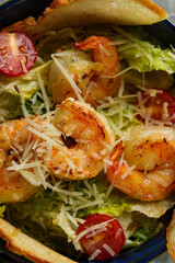 Glistening shrimp sit atop crisp lettuce and juicy tomatoes, all sprinkled with cheese, creating a vibrant dish enjoyed under a clear blue sky during midday