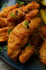 Deep-fried fish fillets sit golden and crispy on a blue plate, adorned with green herbs and accompanied by fresh lemon wedges, evoking a delightful meal experience