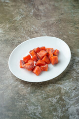 Bright orange cubes of fresh salmon rest elegantly on a round white plate. This vibrant display is perfect for sushi preparation, gourmet salads, or savory entrees