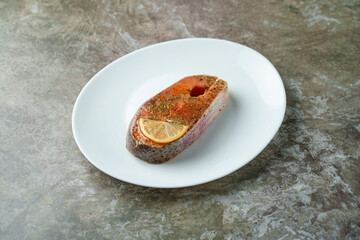 A beautifully grilled salmon fillet rests on a sleek white plate, garnished with a slice of lemon. This dish exudes warmth and flavor, perfect for a family meal at home