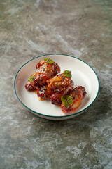 Juicy chicken wings are coated in a vibrant, tangy glaze, sprinkled with sesame seeds, and adorned with fresh green herbs on a vintage-style plate. A feast for the senses