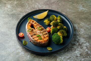 A beautifully prepared dish features grilled salmon with perfectly charred edges, vibrant green broccoli, sweet cherry tomatoes, and a wedge of lemon for zest
