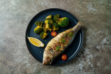 A beautifully presented grilled fish lies on a sleek black plate, accompanied by fresh green...