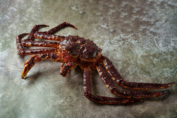 A striking king crab lies on a rugged surface, its large claws and spiky shell glistening in natural light. The vibrant red and brown hues create a captivating visual texture