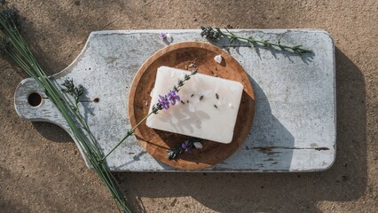 Aloe vera soap with lavender, on a rustic cutting board and white wooden board, surrounded by lavender and green leaves, on a sandy background.
