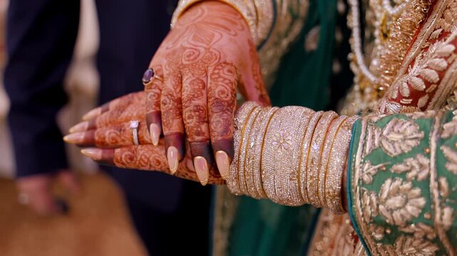 Close up view of Traditional Indian or Pakistan henna painted bridal hands with wedding ring. Bride observing her bangles on the hands