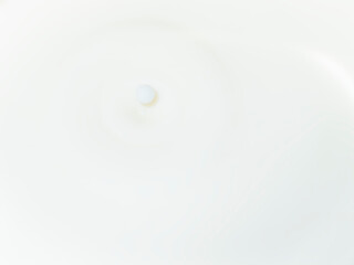 A single drop falls into a smooth, white liquid (milk), creating a subtle ripple. The image captures the subtle elegance of still movement. Minimalist concept.