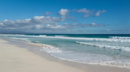 Fototapeta premium Pristine white sand beach meets turquoise ocean waves under a bright blue sky with scattered white clouds in the distance