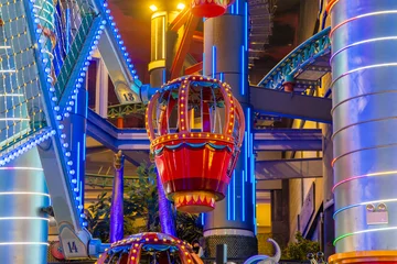 Fototapete Gondeln Hot air balloon gondola illuminates amusement park ride structure with vibrant neon lights. Exciting entertainment and modern leisure concept. Festive, playful atmosphere.  © TravelMedia