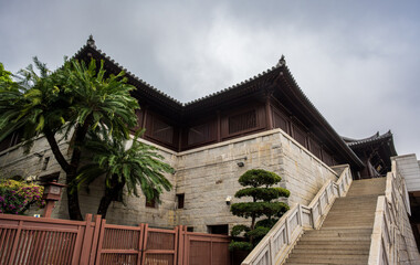 Diamond Hill, Kowloon, Hong Kong : stone stairway leading to Chi Lin Nunnery buildings framed by palm trees and traditional roofs under stormy sky