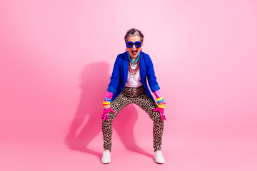 Obraz premium Vibrant retro fashion senior model in blue jacket leopard pants striking playful pose against pink background