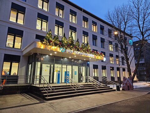 MOSCOW - DEC 19, 2024: Building with a blue sign on the front. The sign says My polyclinic . There are many windows on the medical building with Christmas trees on roof