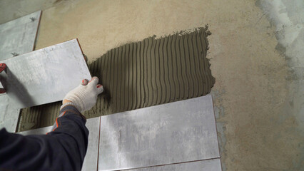 Tiler installing ceramic wall tiles with adhesive