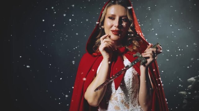 closeup hand holding dagger sharp blade, gothic woman warrior in dark night winter nature old style city street snow falling, fairy lady evil smile. Fantasy girl red hood on head cape white dress 4k