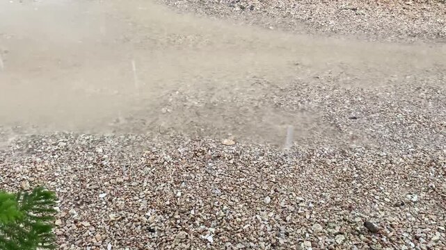 Heavy rain puddled in muddy puddles on the gravel and small rocks covered streets. The water droplets created ripples on the brown surface.
