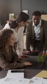 Vertical shot of three biracial colleagues, including Caucasian women and African American man, discussing new report at desk in office