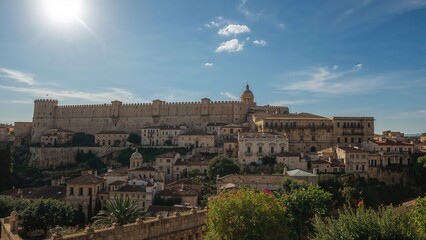 Obraz premium Ancient cityscape with historic buildings and fortress under a bright blue sky with clouds.