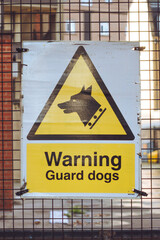 A yellow 'Warning Guard Dogs' sign on a gate