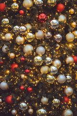 A collection of red, silver and gold baubles nestled in a Christmas tree surrounded by fairy lights