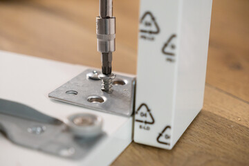 Screwdriver bit precisely fastening a shiny metal screw into a sturdy bracket on white furniture, symbolizing hands-on home improvement and successful furniture assembly