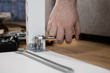 Person's hand using a ratchet screwdriver to fasten a metal bracket securely, actively assembling modern flat-pack furniture at home, showcasing DIY and construction