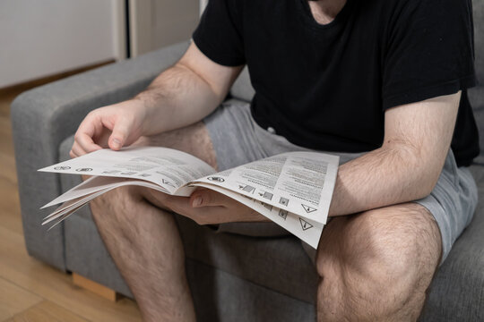 Adult male focused on reading a detailed instruction manual booklet, showing various warning symbols for new product assembly and safe domestic usage