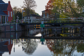 Fototapeta premium Metal drawbridge and traditional brick houses in Bedum, Netherlands. The entire scene reflects in the calm canal water in warm, evening light