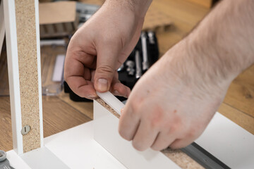 Person's hands carefully inserting white plastic dowel into modern particle board furniture, symbolizing home assembly, DIY skill, and interior design setup