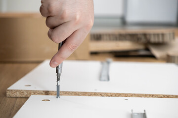 Person's hand uses a screwdriver to assemble new flat-pack furniture, illustrating DIY home...
