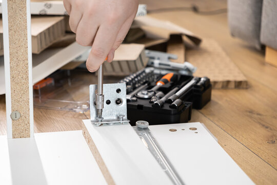 Person's hand fastening a metal bracket with a screwdriver during flat-pack furniture assembly, representing practical home improvement and DIY renovation projects