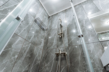 compact shower cabin with grey marble walls and glass partition, chrome mixer and handheld spray,...