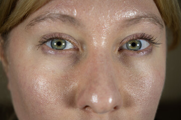 Close-up view of a person with green eyes and a clear complexion indoors, observing the camera during a daytime scene