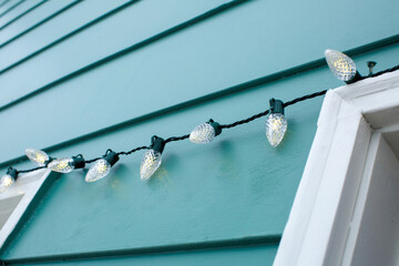 holiday christmas lights hang on side of blue house in winter