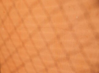 The wall is orange. There are small cracks on the surface and a shadow from the grid. Texture and background. The old wall.