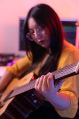 Fototapeta premium Lifestyle image of a woman enjoying acoustic guitar practice indoors, surrounded by a modern workspace and music equipment.