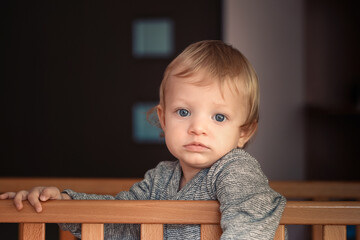 A baby is sitting in a crib with a blue shirt on