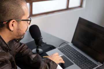 A man speaks into a microphone while streaming from his computer, interacting with digital content in a home indoor setup focused on audio and technology.