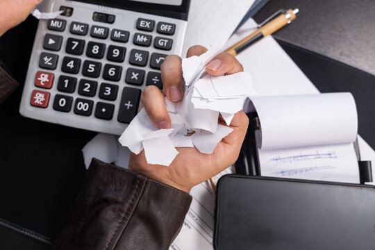 Man sitting at an office desk destroying bills and financial documents, expressing intense stress and anger caused by debt, surrounded by work tools and paperwork.