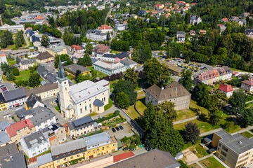 Fototapeta premium Aerial drone view of Jesenik town in Czech Republic showcasing the central market square and historic buildings nestled in Jeseniky Mountains, panoramic urban landscape in sunny summer day