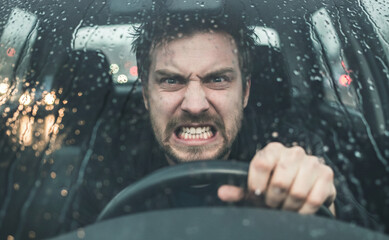 Gros plan sur un conducteur en col&egrave;re serrant le volant, les dents serr&eacute;es, derri&egrave;re un pare-brise mouill&eacute;