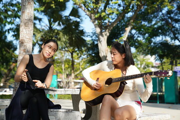 Young woman relaxing in park to do recreational activities, such as playing acoustic guitar in a park.