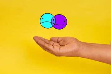An emotional balance concept represented by a hand presenting two overlapping faces expressing contrasting moods.
